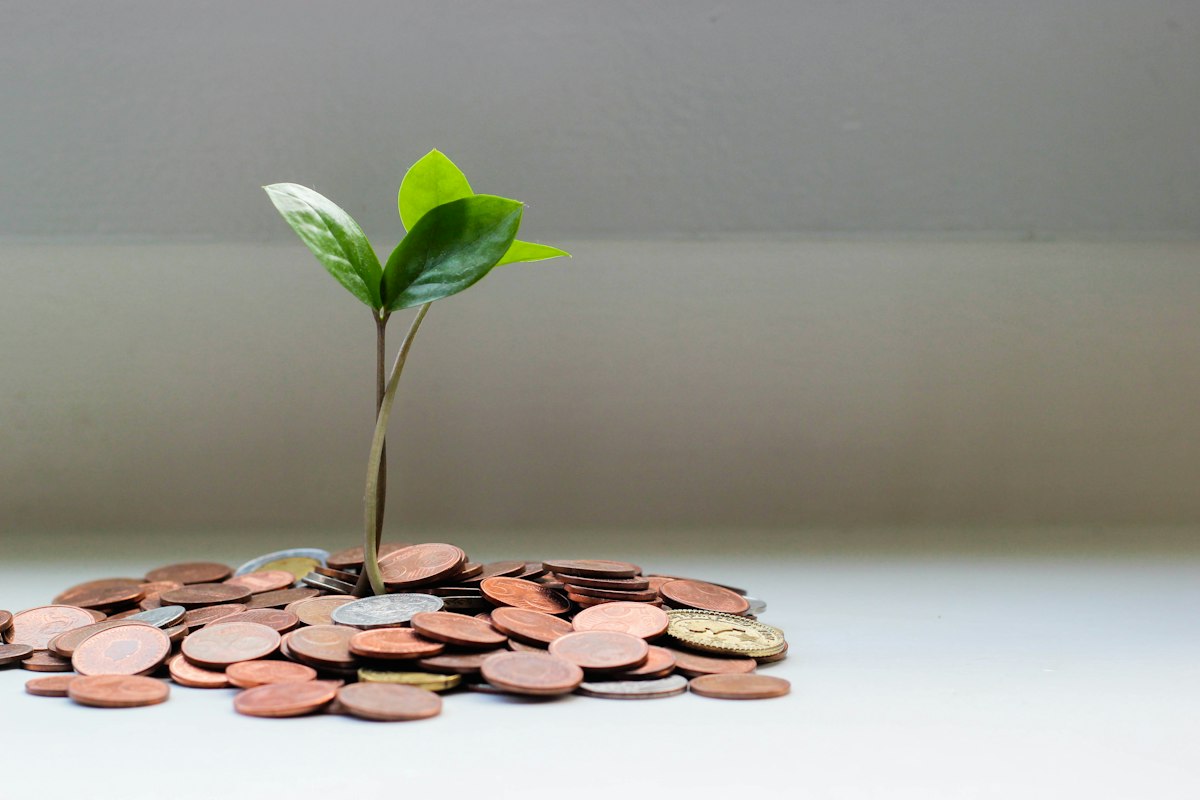 A glass jar of saved coins beside a printed savings goal chart, illustrating long-term saving discipline.